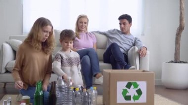 Daha fazla geri dönüşüm için çöpleri ayıran mutlu Kafkas ailesi. Ablam ve abim, çevre dostu olsun diye boş plastik şişeleri geri dönüşüm kutusuna koyuyorlar. Çevre kavramı kaydediliyor.
