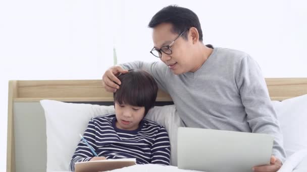 在家工作 快乐的亚洲父亲在家里的卧室里一起坐在床上 一边用笔记本电脑 一边和儿子聊天 社会疏离自我隔离 — 图库视频影像