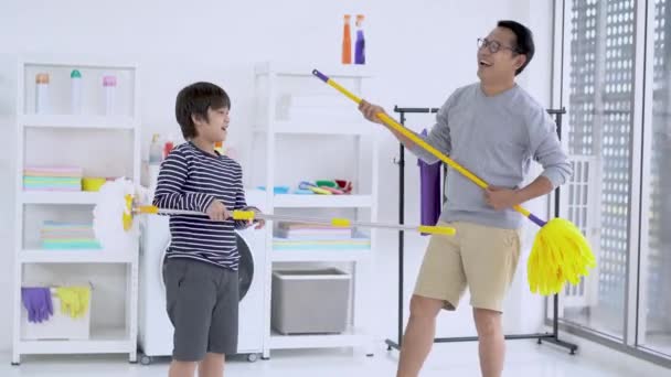 年轻快乐的形象 亚洲父亲和儿子在房间里打扫家 玩拖把和扫帚 料理家务和打扫家的概念 在洗衣房做音乐会 — 图库视频影像