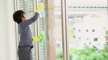 Temizlik ürünlerini spreyleyerek ve süngerle silerek koruyucu eldiven giyen Asyalı bir çocuk. Aile işleri ve ev işleri..