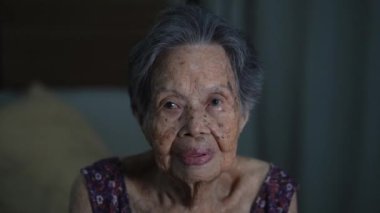 Portrait of elderly Asian woman smiles and waves at the camera in living room at home. Old age, gesture and people concept