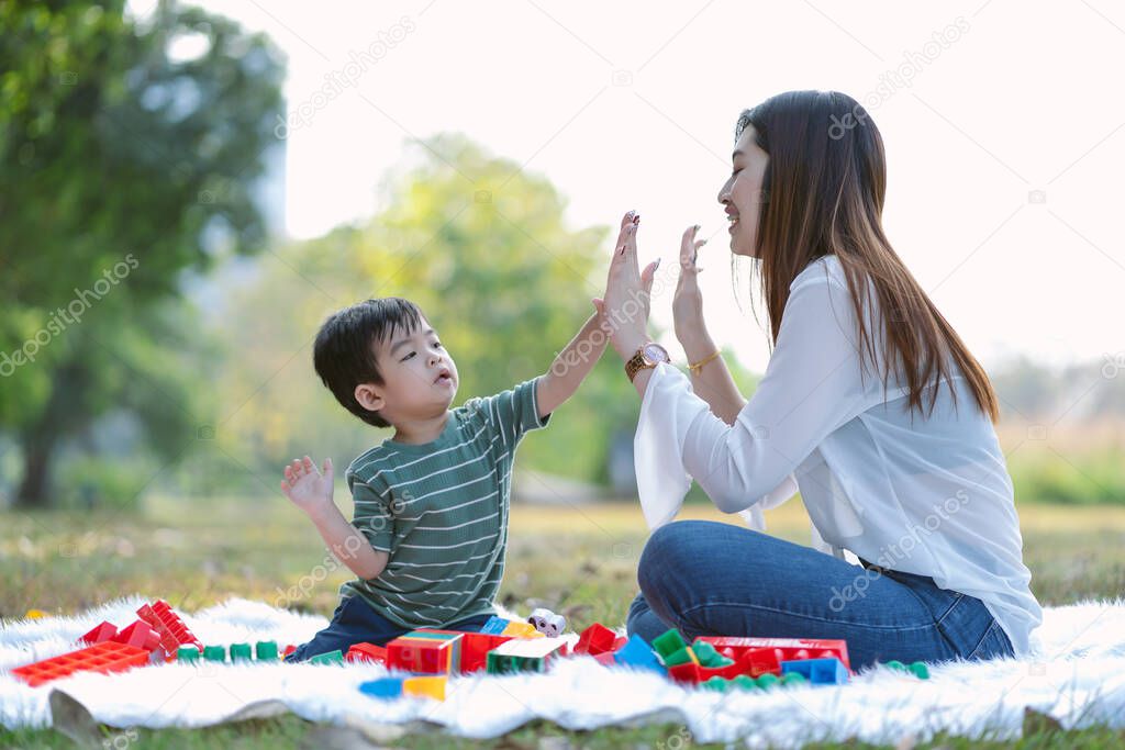 Portrait of happy Asian mother and little son wearing casual style give high five and playing together in the park. Family, Kid spending time relax in holiday.