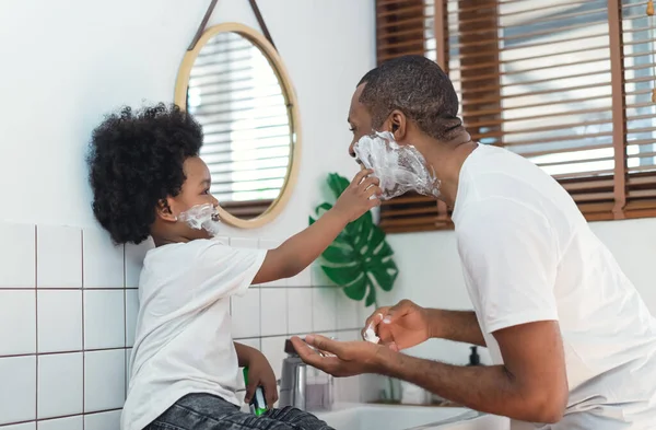アフリカ系黒人の父と小さな息子が顔に泡を剃り バスルームで笑っています 黒人家族は一緒に時間を過ごす 浴室の概念の朝のルーチン — ストック写真