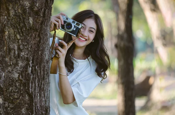 美丽的年轻游客亚洲博客女性的肖像 在公园里的树上 用老式相机开心地微笑着 假日活动和现代生活方式的概念 复制空间 — 图库照片