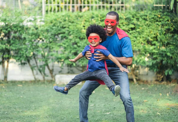 Szczęśliwy Zabawny Afroamerykanin Ojciec Niosący Małego Chłopca Latającego Kostiumie Superbohatera Obraz Stockowy