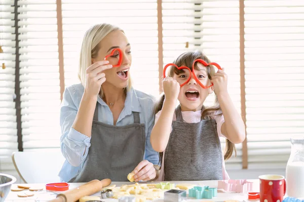 幸せな白人の家族は一緒に台所で楽しい時間を過ごします ママと小さな娘楽しみます保持赤クッキーカッターハート形で眼鏡として 家で面白い写真のためにカメラを見て — ストック写真
