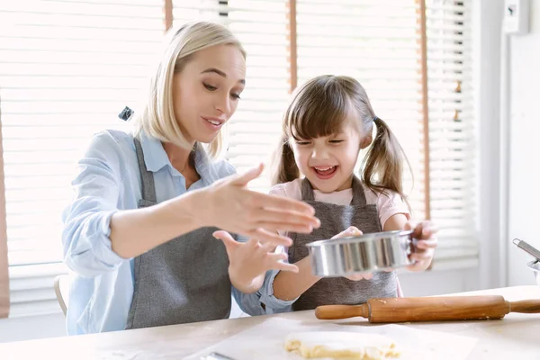 キッチンで一緒に時間を過ごす幸せな白人の家族 美しいお母さんは世話をし 家で台所でパン屋を作るために小麦粉で生地を振りかけるのを助ける愛らしい娘を教えています — ストック写真