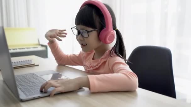 可愛いアジア系の女子高生がリビングでノートパソコンを使ってビデオレッスンをしています 面白いかわいい女の子と言うこんにちはとダンスに先生や友人にオンライン学校教育に家で — ストック動画