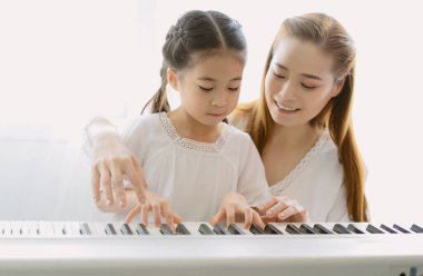 Anne Asyalı 'nın evdeki oturma odasında kızına piyano çalmayı öğretirkenki portresi. Hafta sonunu birlikte geçirin, mutlu anne ve kız. Çocuklar için becerileri güçlendirmek için etkinlikler oluşturuluyor.