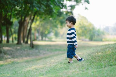 Parkta yürürken ayakta durup gülen sevimli Asyalı küçük çocuğun yan görüntüsü. Pozitif duygular ve enerji. Çocuk parkta gün ışığında.