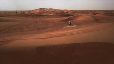 Bisikletle sürüklenen yarışçıyla Dubai Çölü 'nün hava panoramik manzarası. Rub al Khali, Abu Dabi, BAE. 4K, görüntüler.