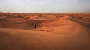 Bisikletle yola çıkan yarışçıyla Dubai çölünün hava panoramik görüntüsü. Rub al Khali, Abu Dabi, UAE.4K, kamera görüntüleri.