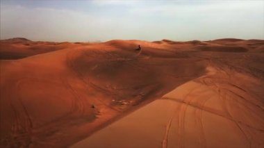Bisikletli bir yarışçıyla Dubai Çölü 'nün hava panoramik manzarası. Kum tepesinde sürüş ve duruş. Rub al Khali, Abu Dabi, UAE.4K