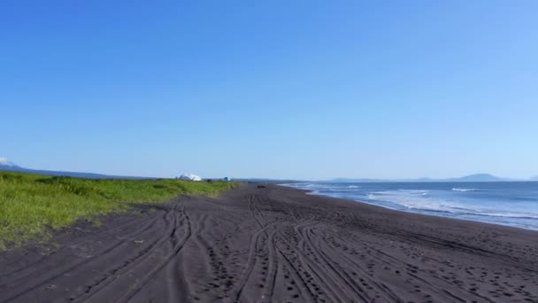 Paysage aérien de la côte islandaise, avec des empreintes de pas dans le sable menant à des cavaliers à cheval, à côté d'un camp sur la pelouse — Video