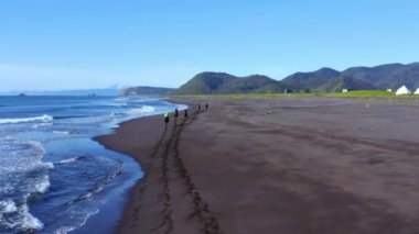 Az bilinen kumlu bir sahil şeridinin havadan manzarası. Atlı atlılar deniz boyunca dört nala koşuyor, İzlanda.