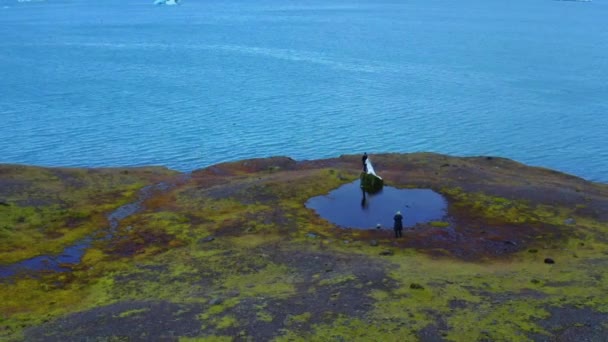 Widok z lotu ptaka na dwóch nowożeńców i kamerzystę na skraju brzegu — Wideo stockowe