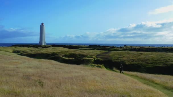 Girl walking the grass path to the lighthouse in the field on a cliff of Iceland — Stockvideo