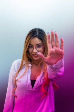 Gözlüklü, gülümseyen kadının renkli arka planda dururken avuç içini göstermesi.