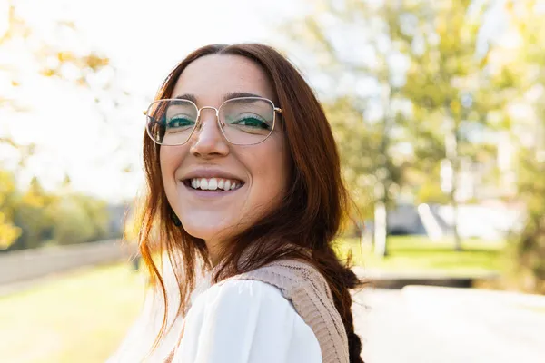 Portré gyönyörű fiatal nő szemüveggel, vörös haj és szeplők mosolygó nézi a kamera a parkban. Természet, emberek és boldogság fogalma — Stock Fotó