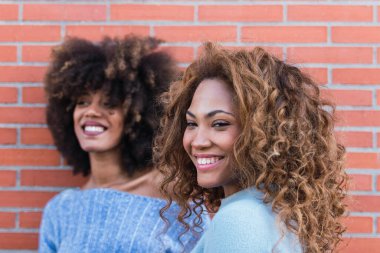 Gülümseyen, uzun kıvırcık saçlı, göz kamaştırıcı makyajlı ve mavi kazaklı Afro-Amerikan kadın. Afro saç stiliyle gülen Afrikalı doğal kızların güzel portresi. Seçici odak