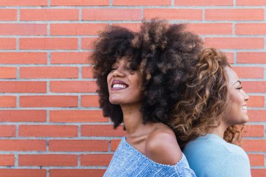 Tuğla duvarda poz veren uzun afro saçlı ve göz alıcı makyajlı gülümseyen Afro-Amerikan kadınları. Afrikalı doğal kızların güzel portresi fotokopi aletiyle arka arkaya duruyor.
