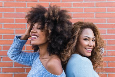 Uzun afro saçlı, parlak makyajlı ve mavi gömlekli, duvara poz veren gülümseyen Afro-Amerikan kadınları. Sırt sırta duran Afrikalı doğal kızların güzel portresi