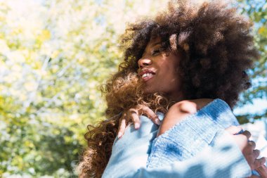 Two female afro american friends and happy best friends hugging each other and laughing in the park. Cheerful afro black friends with curly hair smiling with love and giving warm hug