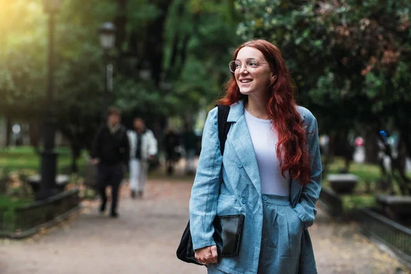 Vonzó fiatal üzletasszony kék öltönyt visel digitális táblagép a szabadban, profi női építész sétál a parkban, fáklya fény — Stock Fotó