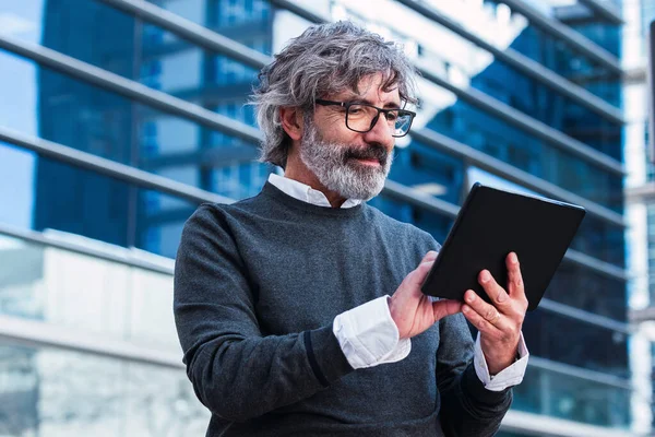 Ofis binasının önünde dijital tablet kullanan olgun, yakışıklı bir iş adamı.