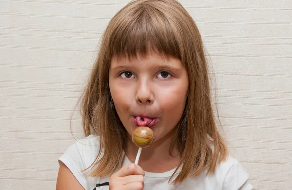 Liten flicka poser och slicka lollypop — Stockfoto