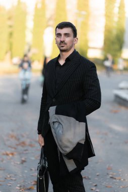 Genç işadamı bir palto tutuyor ve sokakta duruyor.