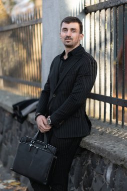 Avukat beton bir çite yaslanmış oturuyor, işten dinleniyor.