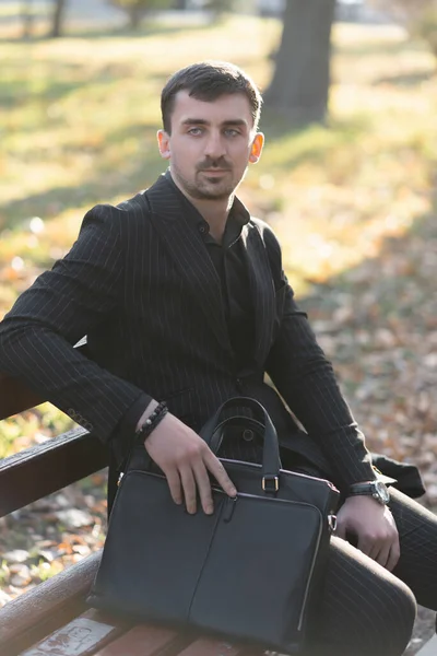 Bir ofis çalışanı parktaki bir bankta çantasına oturmuş yarım kalan işini düşünüyor.