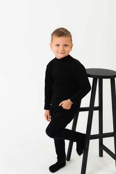 Um menino de pé ao lado de uma cadeira com a mão no bolso e olhando para a câmera e sorrindo — Fotografia de Stock