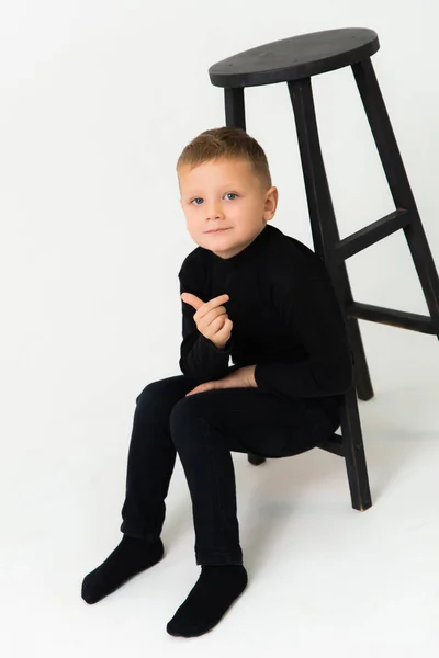 Um menino está sentado ao lado de uma cadeira e mostrando seu polegar. — Fotografia de Stock