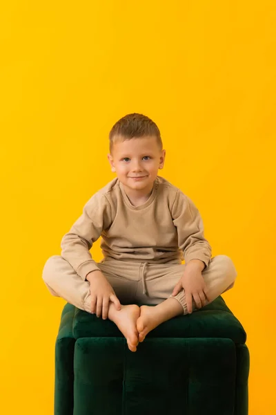 Um menino sentado em um sofá contra fundo amarelo olhando para a câmera, com espaço de cópia para um ponto de vista — Fotografia de Stock