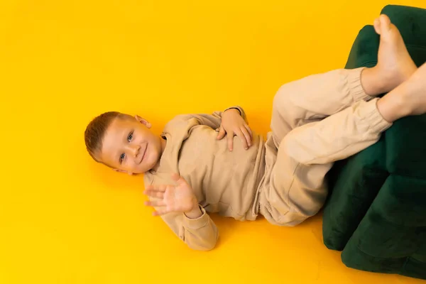 Um menino está cumprimentando deitado de costas em um estúdio em um fundo amarelo — Fotografia de Stock