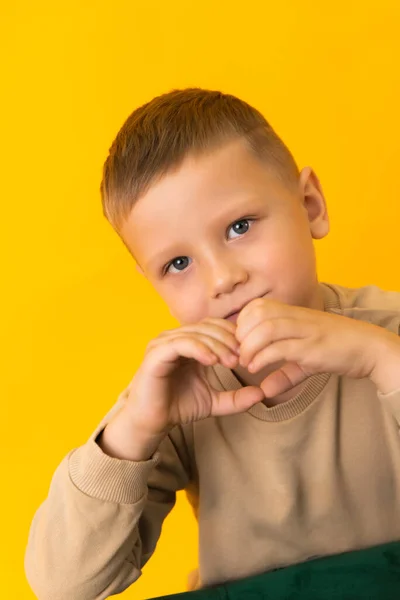 Um menino loiro mostrando o coração de suas mãos e olhando para a câmera — Fotografia de Stock