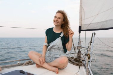 Çekici, gülümseyen bir kadın yatta otururken kameraya bakıp kızıl saçlarına dokunuyor. Seyahat, turizm ve yaz konsepti