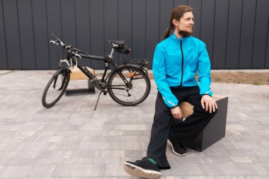 Bankta oturan sakallı bir adam Bisikletin yanında ve yan bakıyor