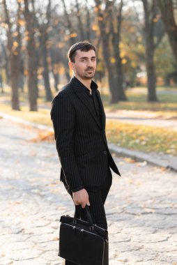 Siyah takım elbiseli genç bir işadamı sokakta yürüyor.