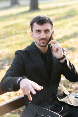 Bir işadamı telefonda konuşuyor, kameraya bakıyor ve elleriyle işaret ediyor.