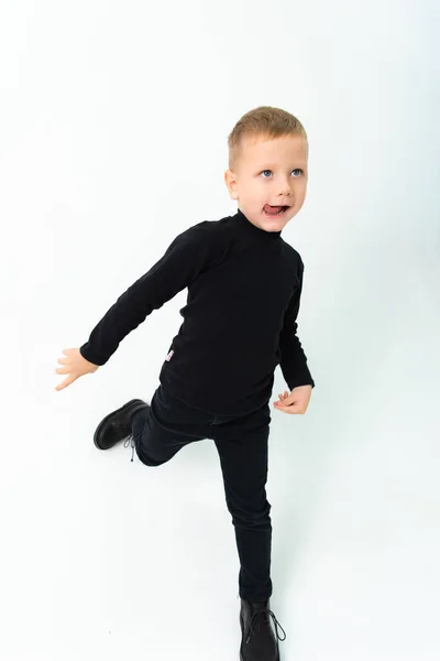 A blond boy in black clothes is showing his tongue while taking pictures in a studio — Fotografia de Stock