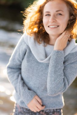 Kızıl saçlı bir kızın portresi kameraya bakıyor ve gülümsüyor.