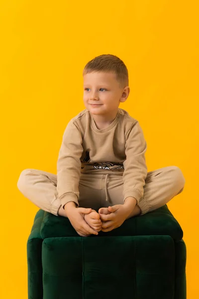 Small boy sitting cross-legged smiling on yellow background — Fotografia de Stock