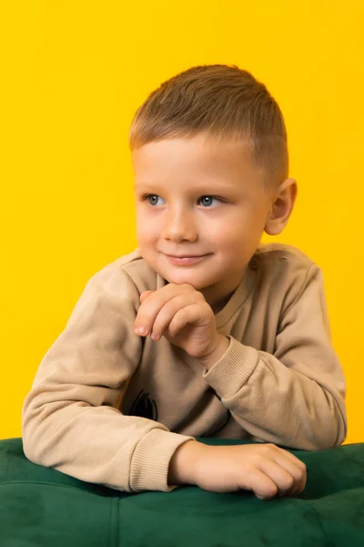 A little smiling boy is looking to the side on a yellow background in the studio — Fotografia de Stock