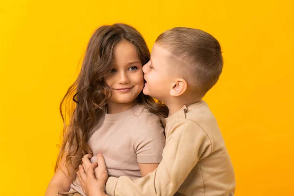 Ein jüngerer Bruder umarmt und küsst seine ältere Schwester auf gelbem Hintergrund im Studio — Stockfoto