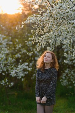 Bahçede çiçek açan elma ağaçları olan güzel, genç bir kadın. Gülümseyen kadın eğleniyor ve eğleniyor