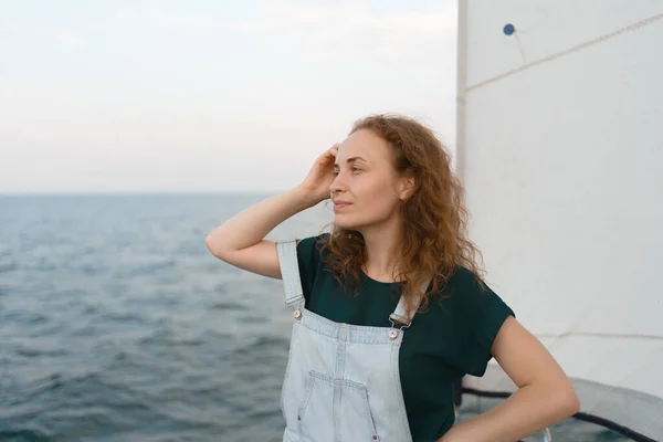 A ginger-hair woman on a yacht on the sea enjoys the sea landscape. The woman on summer vacation enjoying the view of the sea