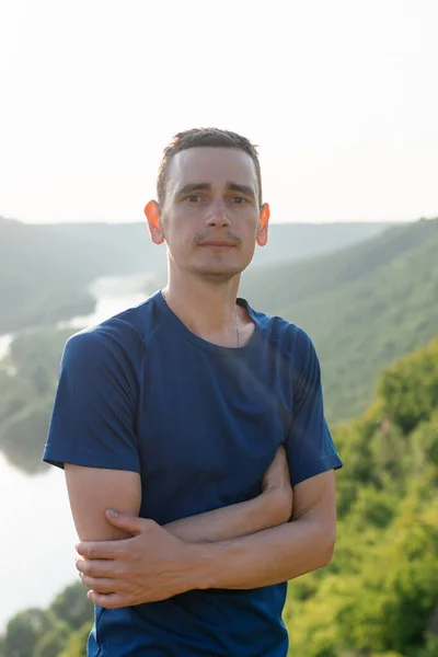 川や森を背景にカメラを見た青いTシャツの若者の肖像 — ストック写真